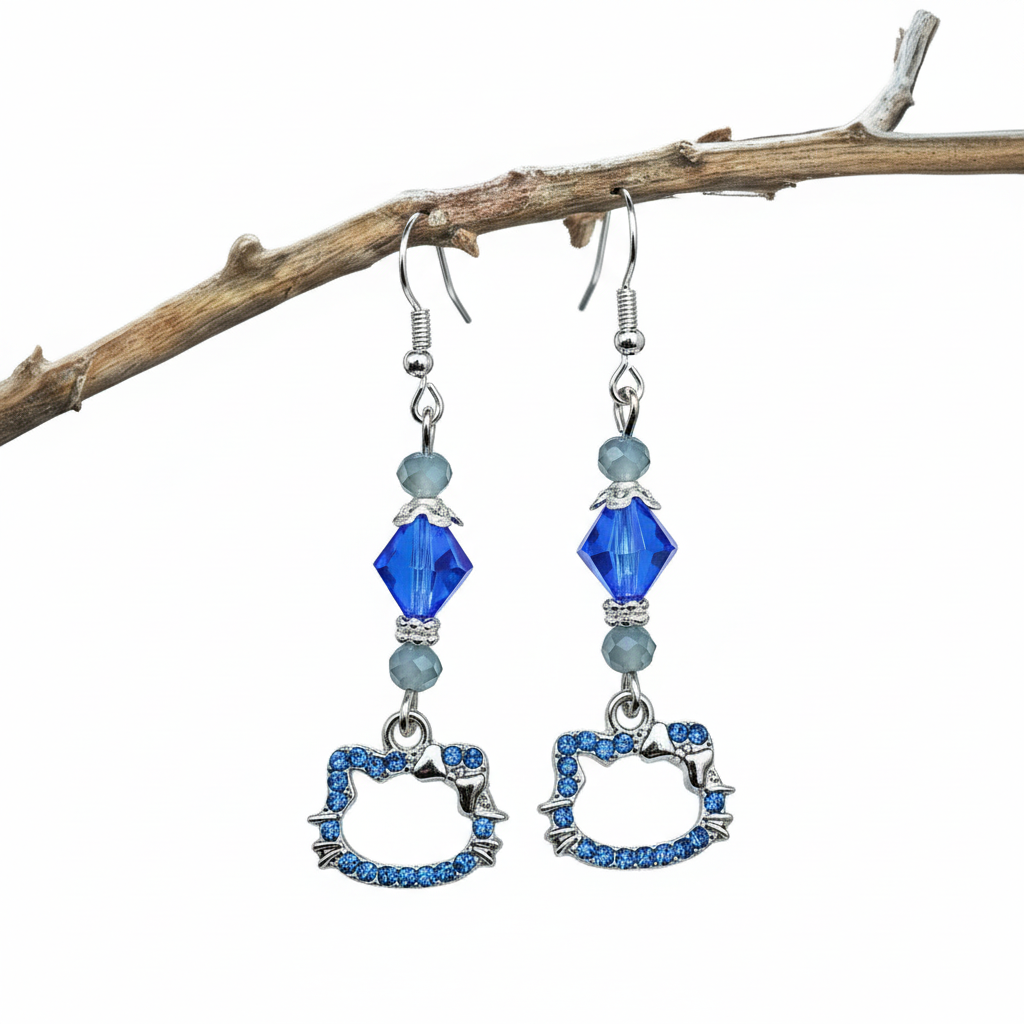 A pair of silver-plated cat charm earrings with blue gemstone or crystal beads, displayed against a marble background with blue and purple flowers.