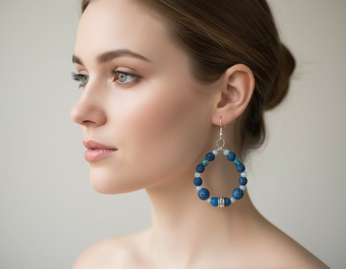 Blue beaded hoop earrings hanging on a branch with a white background