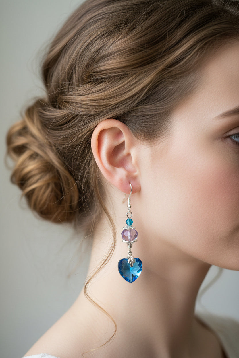 Heart-shaped blue and purple earrings hanging on a branch with a blurred background