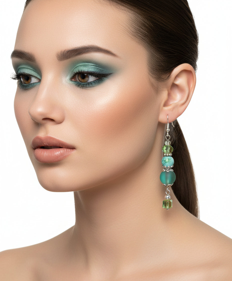 Green beaded earrings on a branch with a white background