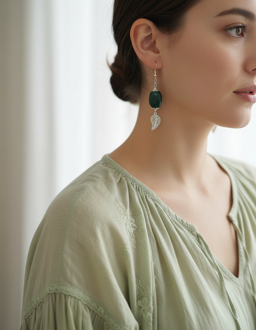 Green earrings with leaf designs hanging from a branch on a white background