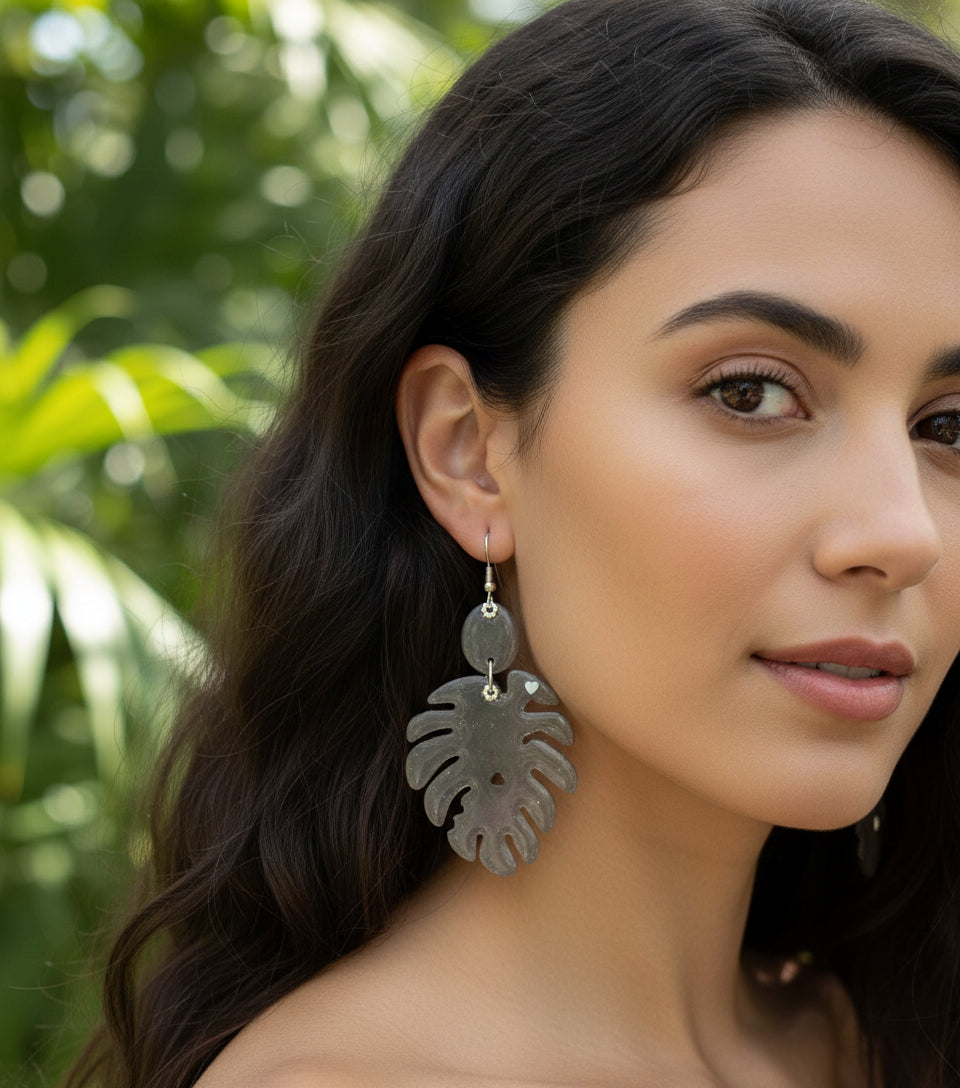Silver leaf-shaped earrings hanging from a branch on a light gray background