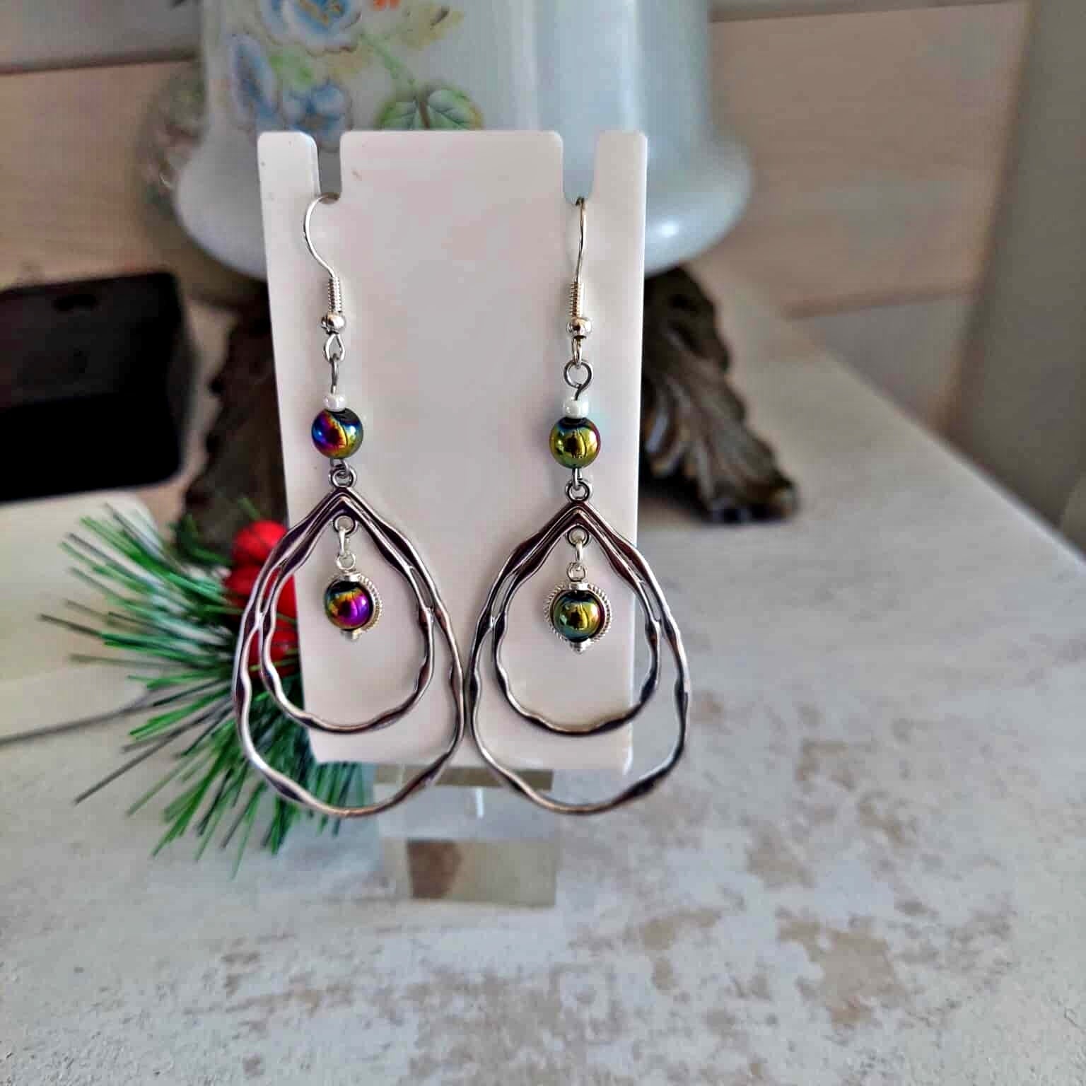 Teardrop-shaped earrings with colorful beads on a white card, blurred background