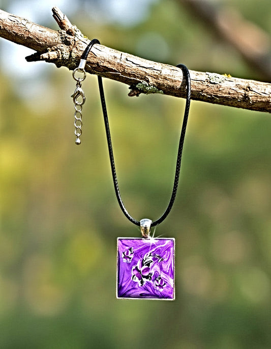 Purple pendant necklace on a black cord hanging from a branch with a blurred green background
