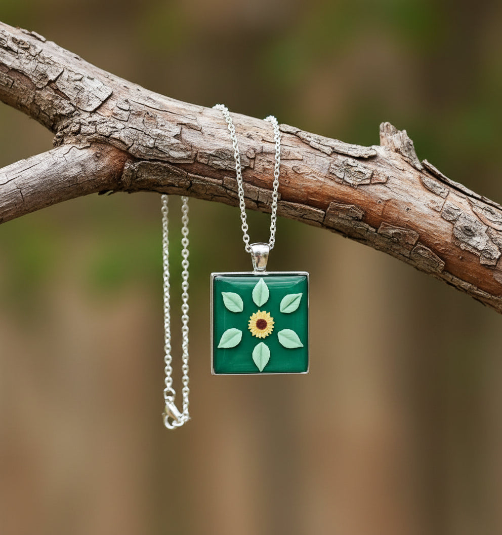 Square pendant with floral design on a green background, attached to a chain on a white background