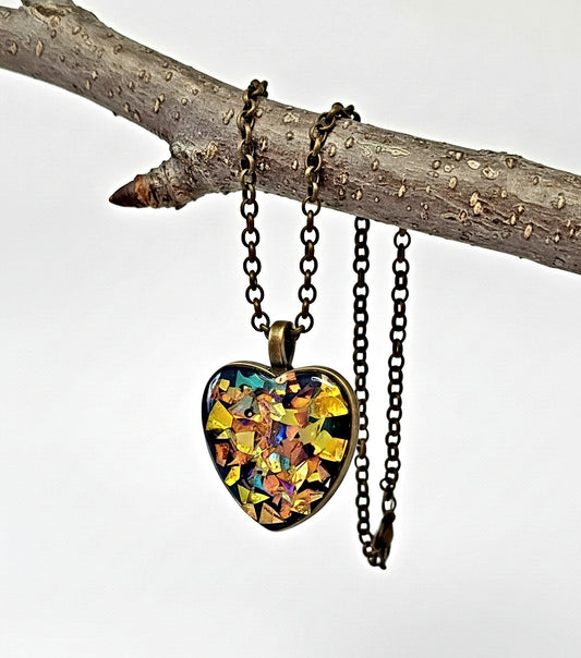 Heart-shaped pendant with multicolored design on a chain, hanging from a branch.
