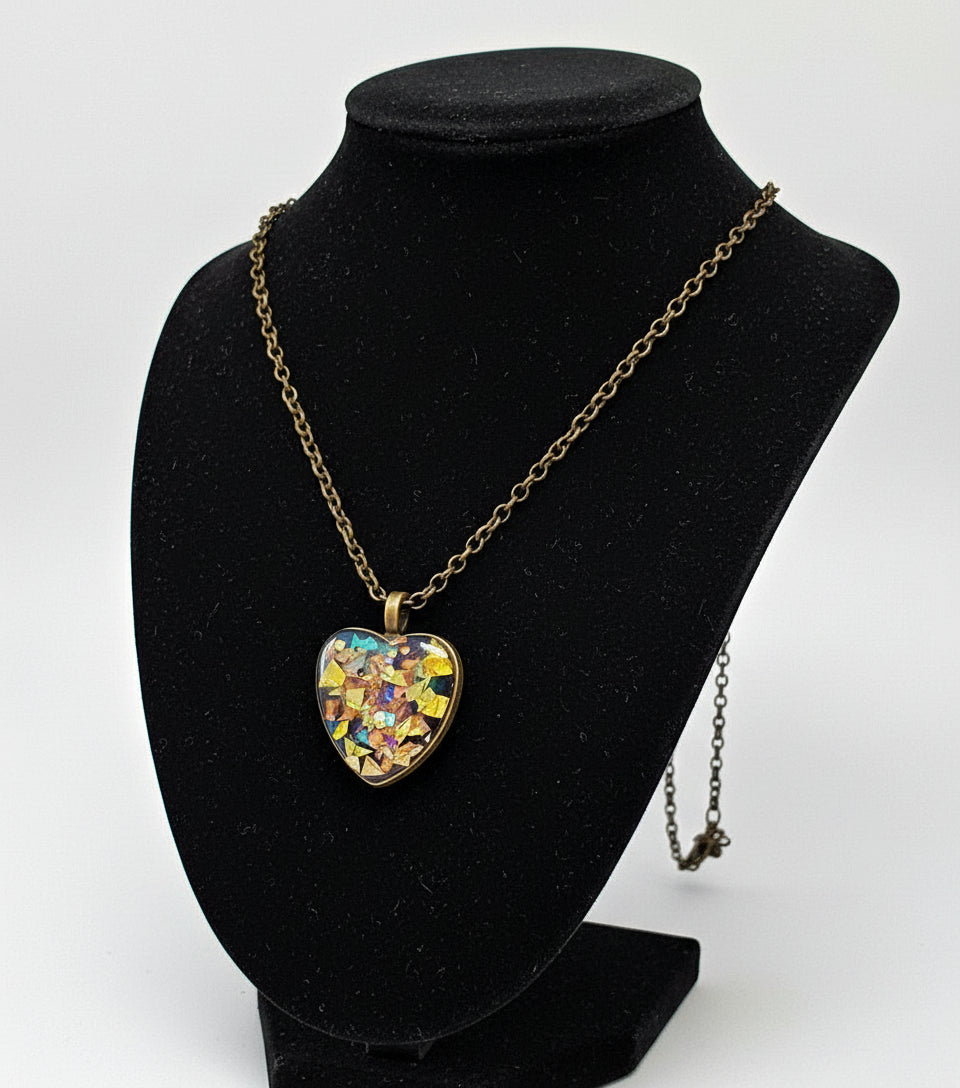 Heart-shaped pendant with multicolored design on a chain, hanging from a branch.