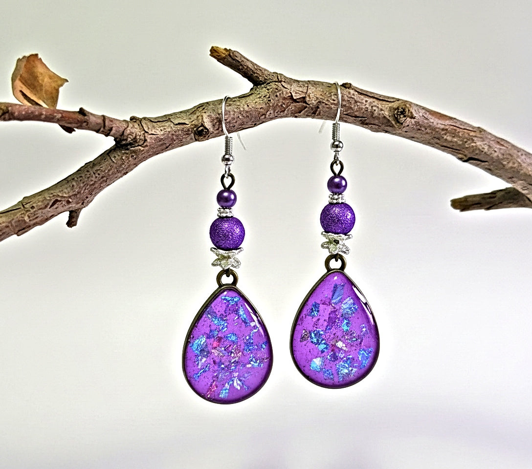 Purple teardrop earrings with beaded accents hanging on a branch.