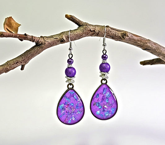 Purple teardrop earrings with beaded accents hanging on a branch.