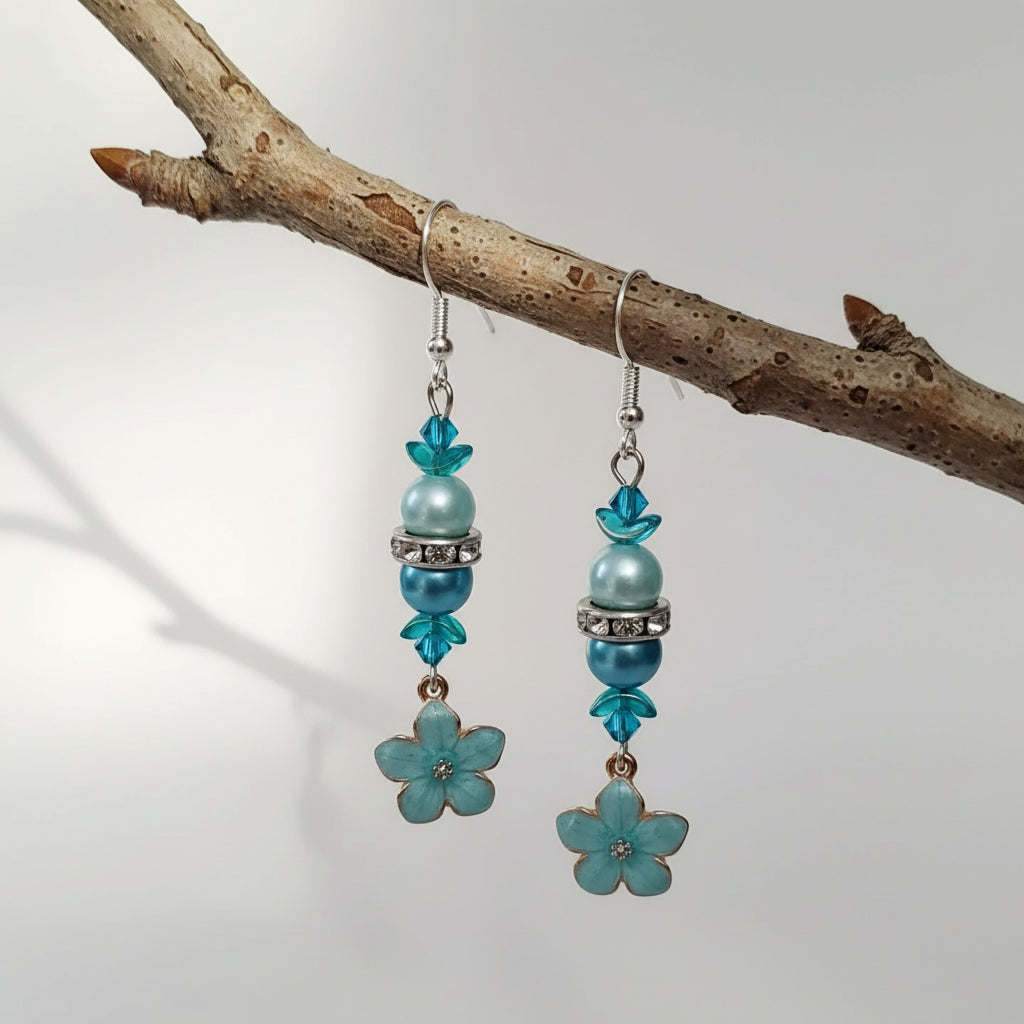 Pair of earrings with blue floral charms and beads on a light gray background