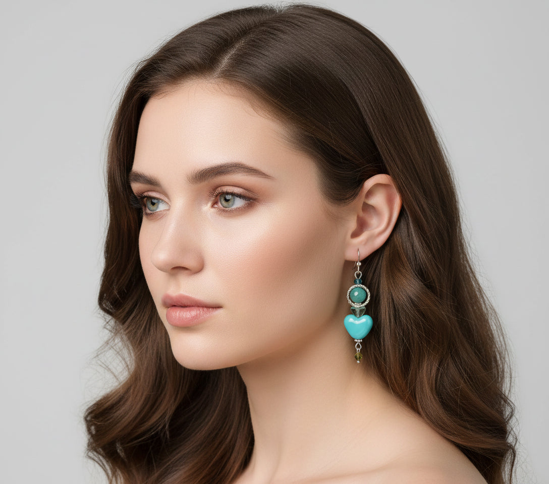 Turquoise heart-shaped earrings with silver and green accents hanging from a branch.