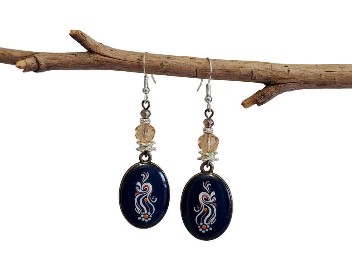 Pair of earrings with blue oval stones and gold beads hanging on a branch.