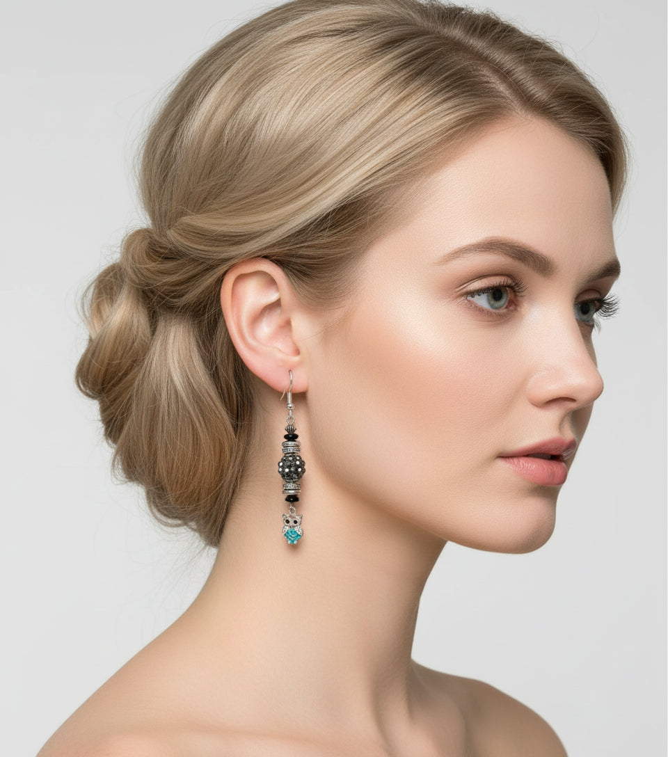 Pair of earrings with owl charms hanging from a branch on a white background