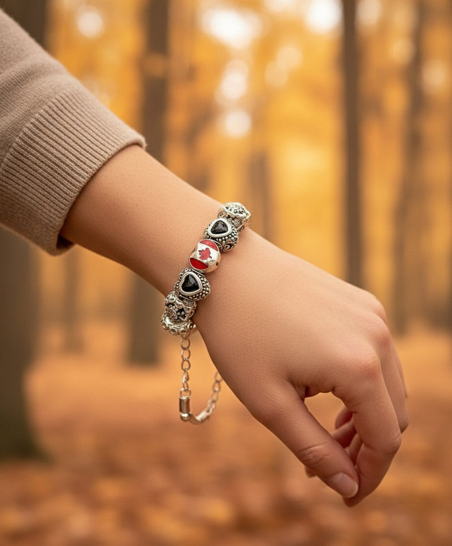 Two silver hoop earrings with heart and Canadian flag charms on a branch with autumn leaves.