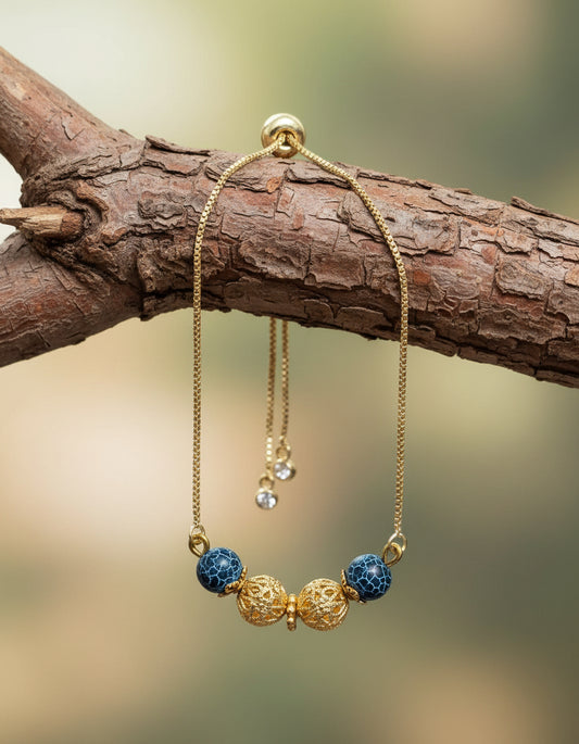 Gold bracelet with blue and gold beads on a gray wooden surface