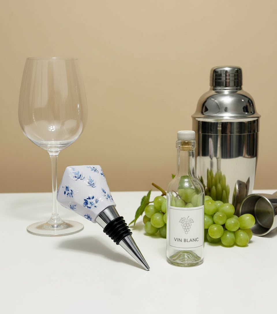 Bottle stopper with floral design next to a small bottle labeled 'Vin Blanc' on a beige background