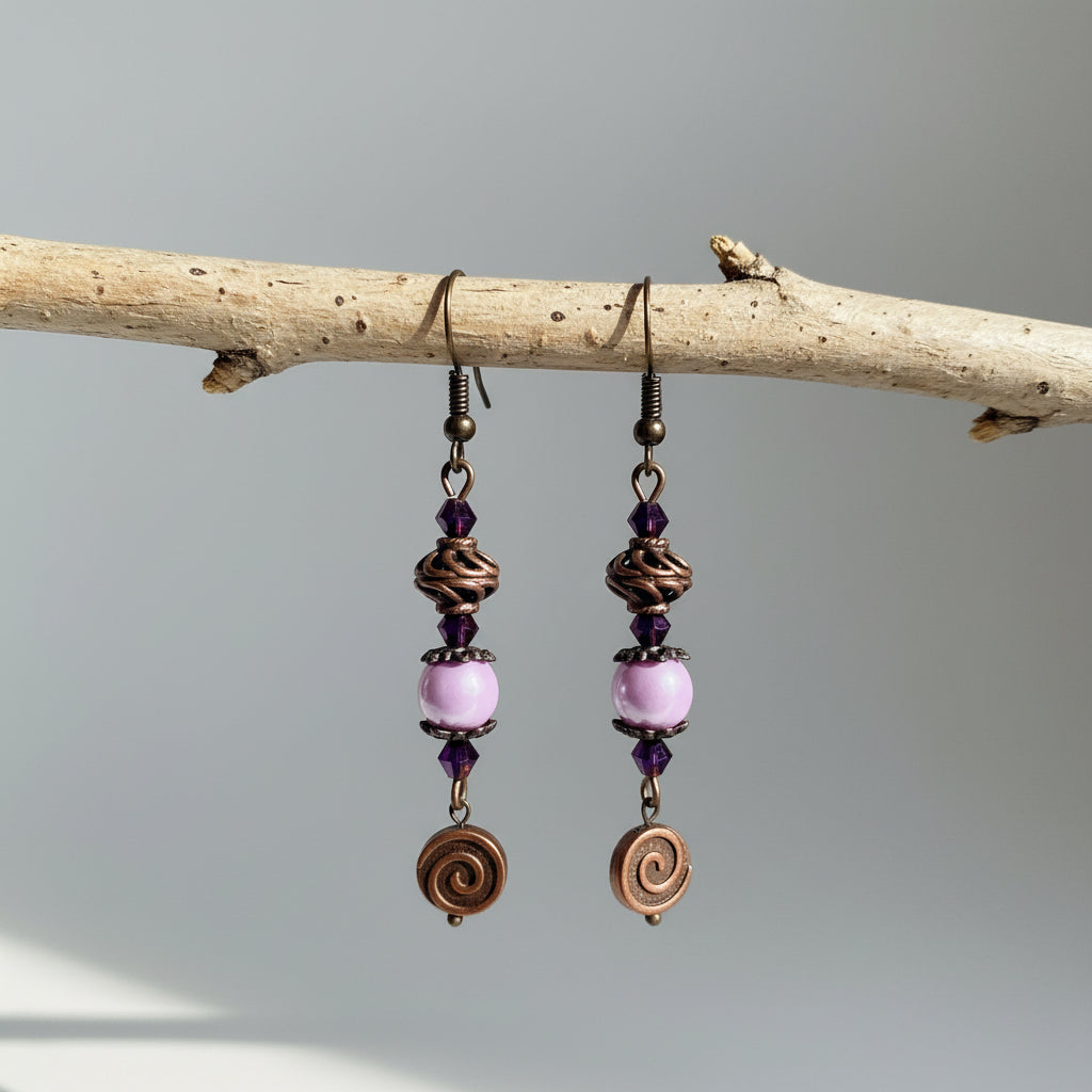 Pair of earrings with pink beads and bronze spiral designs hanging on a branch.
