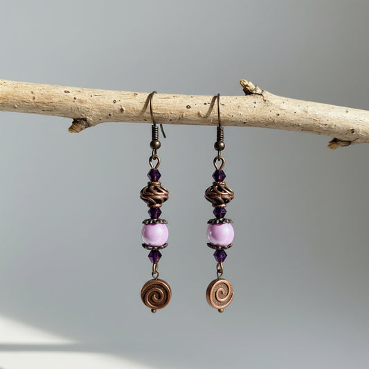 Pair of earrings with pink beads and bronze spiral designs hanging on a branch.