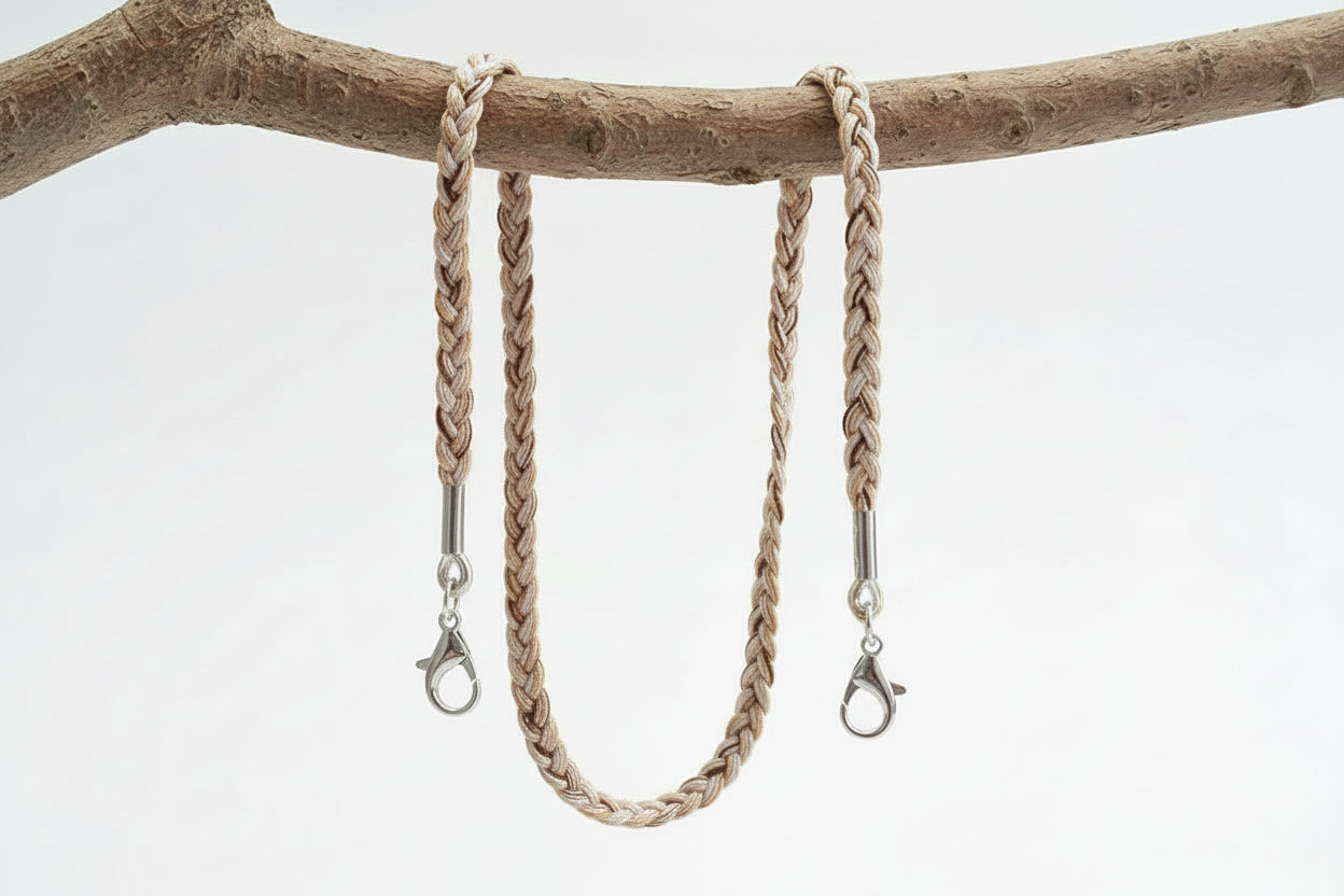 Beige braided necklace lanyard hanging on a branch with a white background