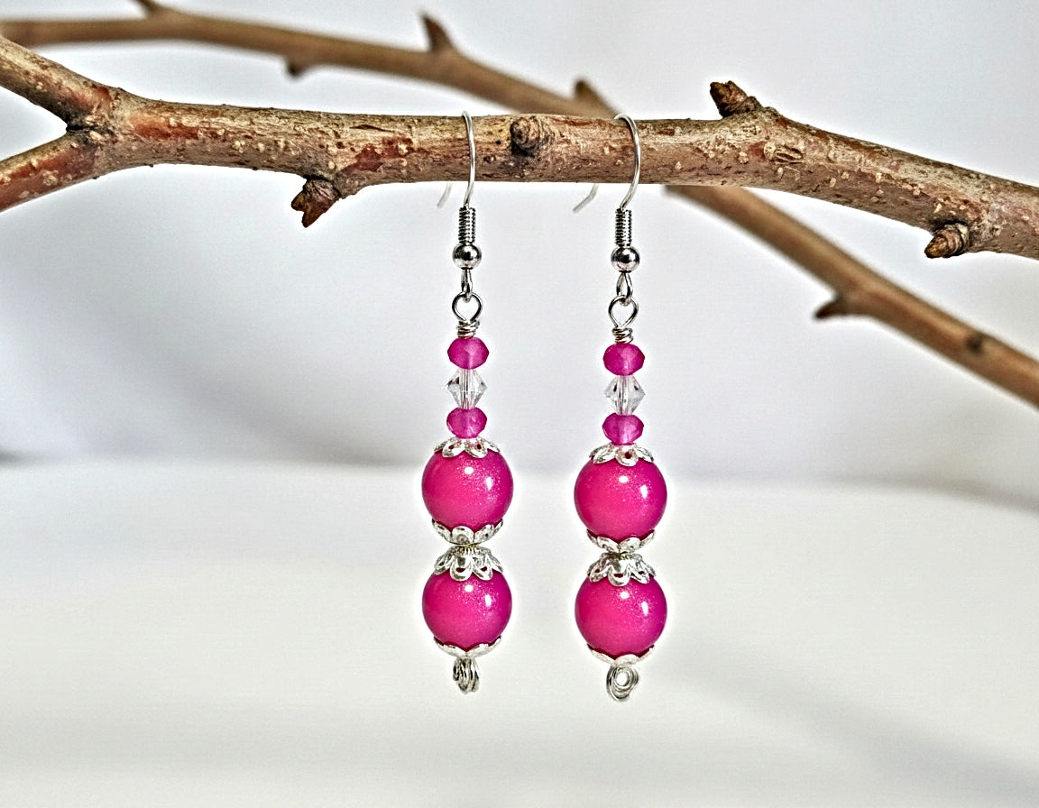 Pink beaded earrings hanging from a branch with a blurred background