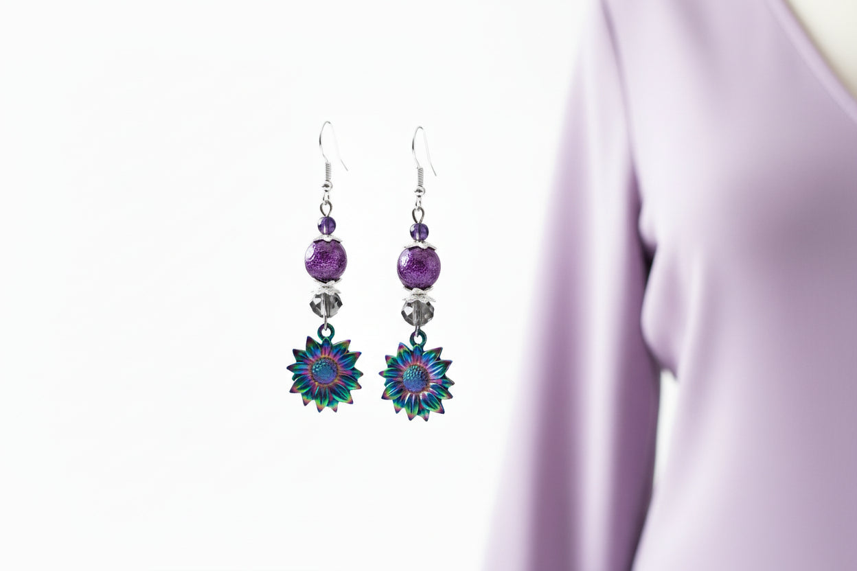 Pair of earrings with floral designs and purple beads hanging on a branch.
