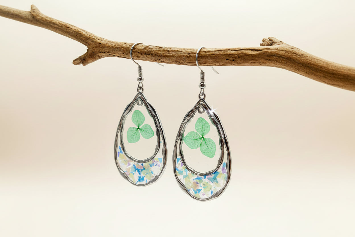Teardrop-shaped earrings with floral designs hanging on a branch against a beige background