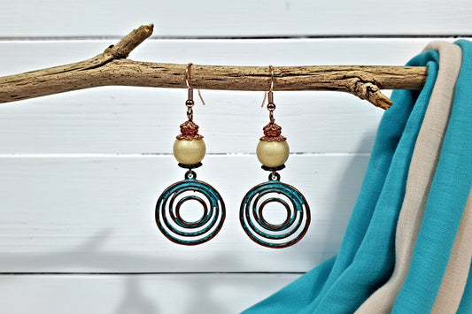 Pair of earrings with circular designs hanging from a branch against a white wooden background