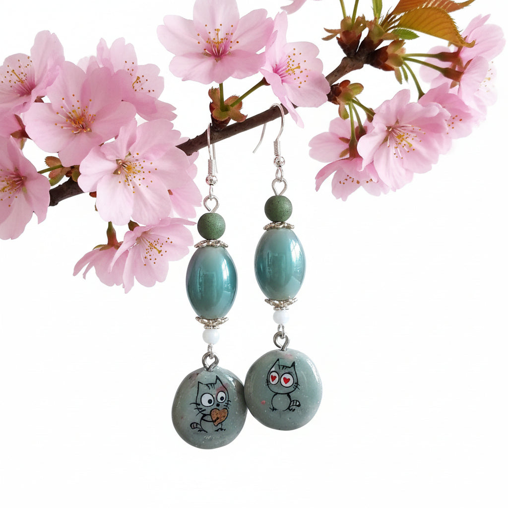 Pair of earrings with cartoon cat charms on a textured fabric background