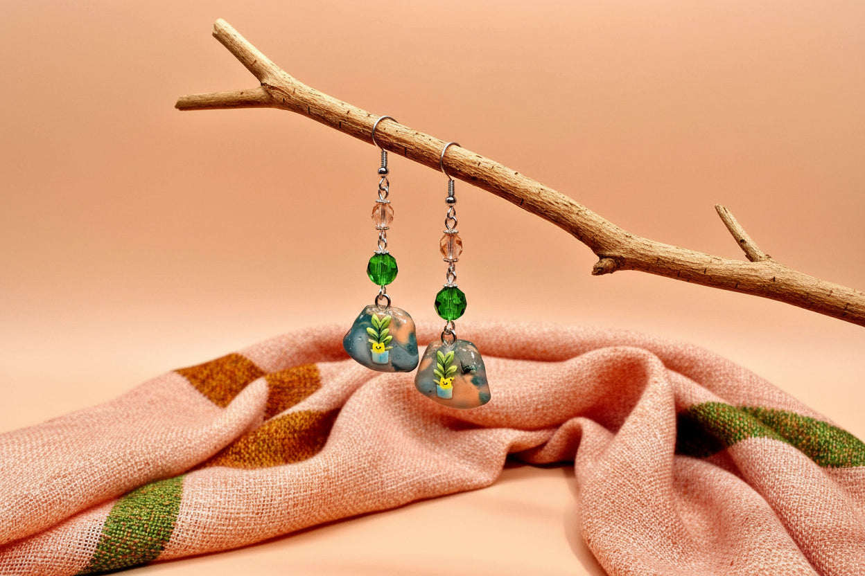 Pair of earrings with green and brown beads hanging on a branch against a peach background