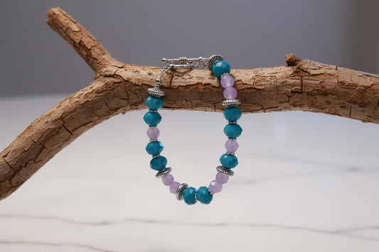 Beaded bracelet with blue and purple beads on a marble surface with a gold stand and dried flowers.
