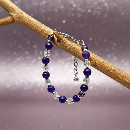 Purple beaded bracelet with silver accents on a branch against a gray background
