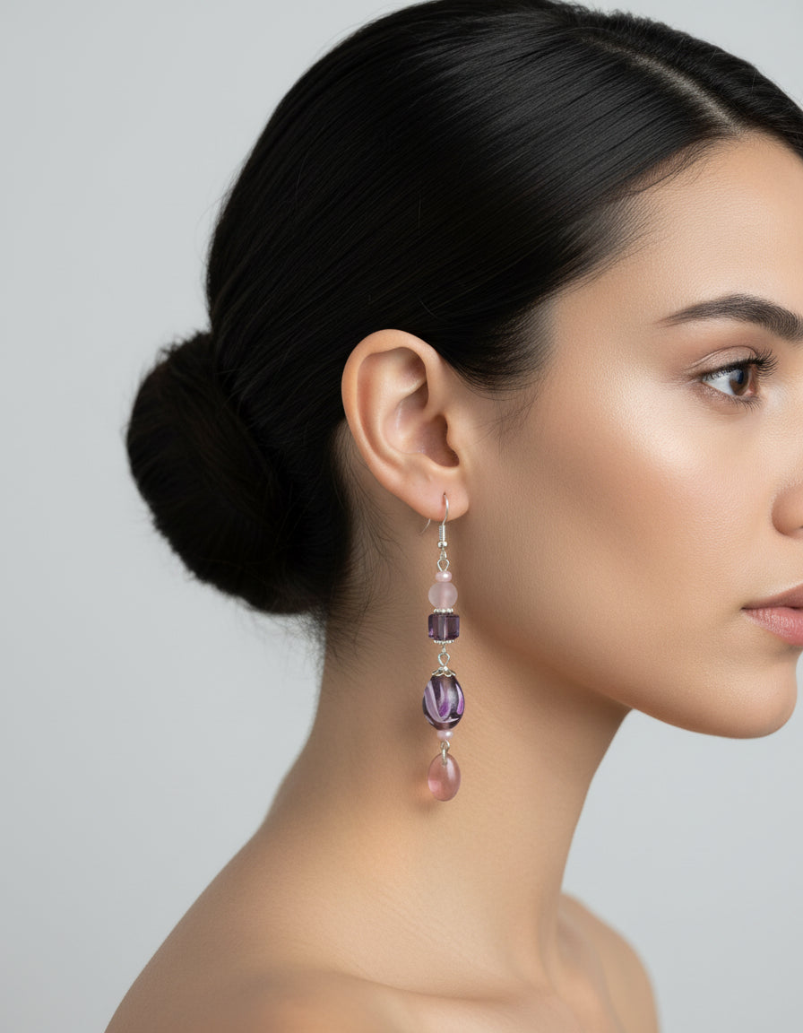 Purple and pink beaded earrings hanging from a branch on a white background