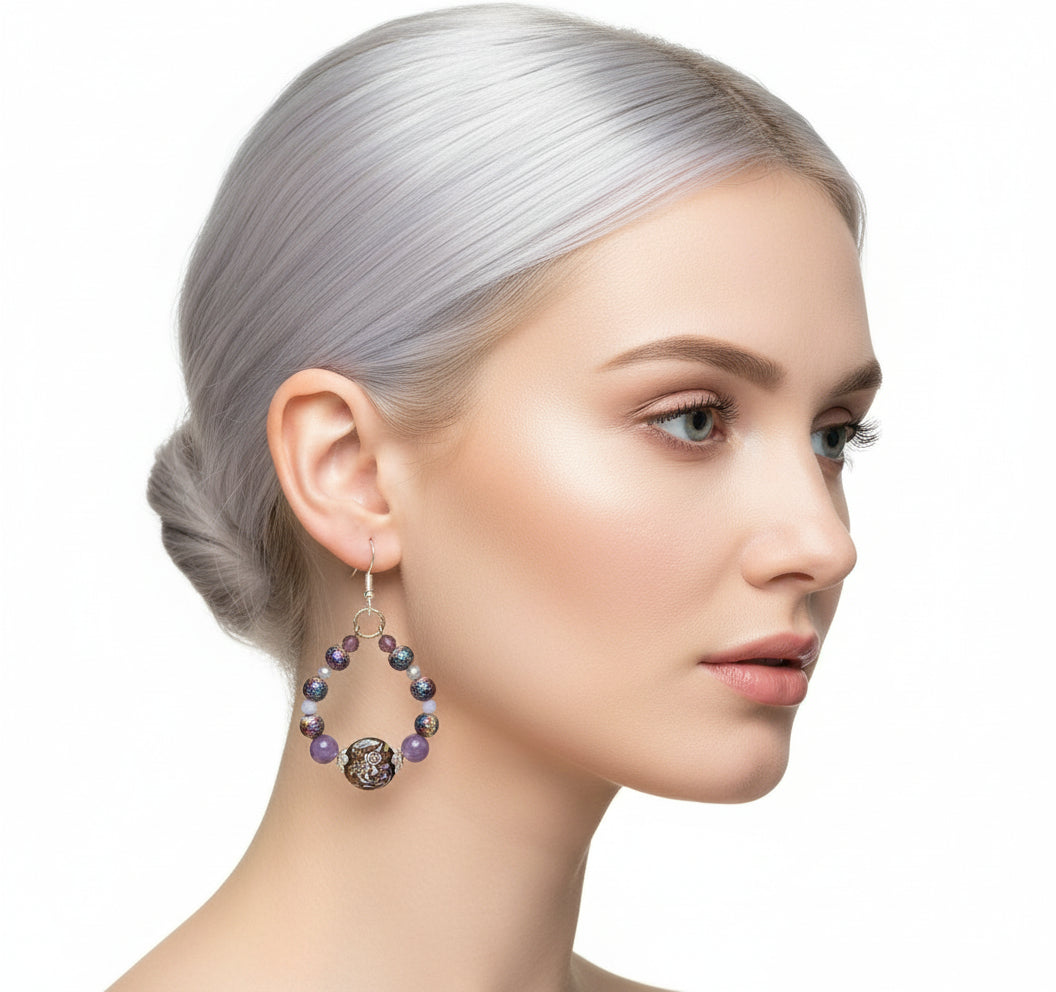 Purple beaded earrings with gold accents on a branch against a white background