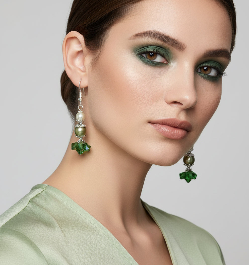 Pair of earrings with green and pearl beads hanging on a branch.