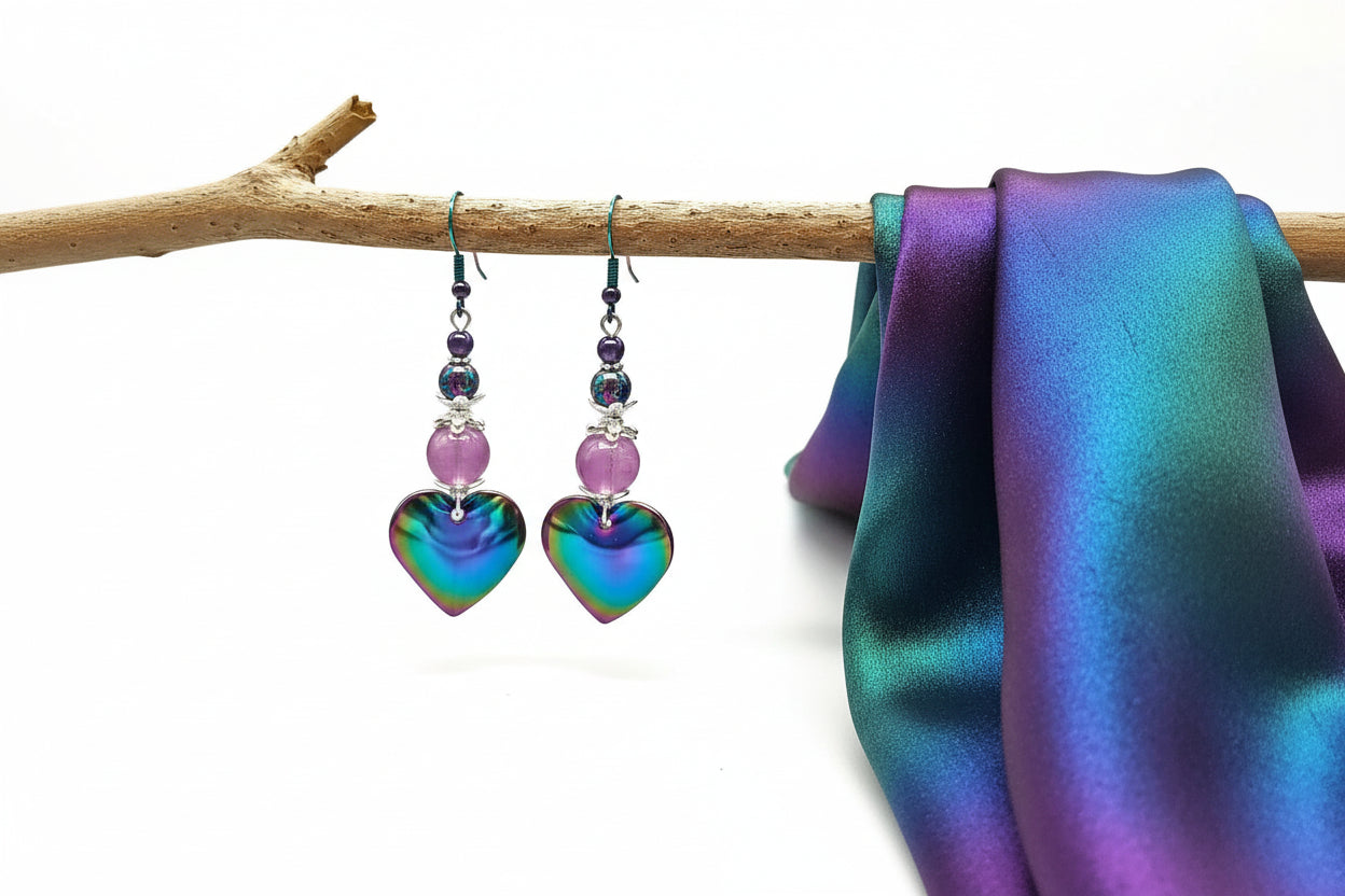 Heart-shaped colorful earrings with purple beads hanging on a branch.