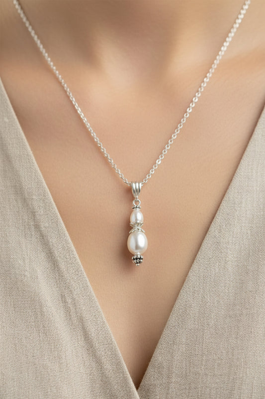 Silver necklace with a pearl pendant on a wooden surface with white flowers.
