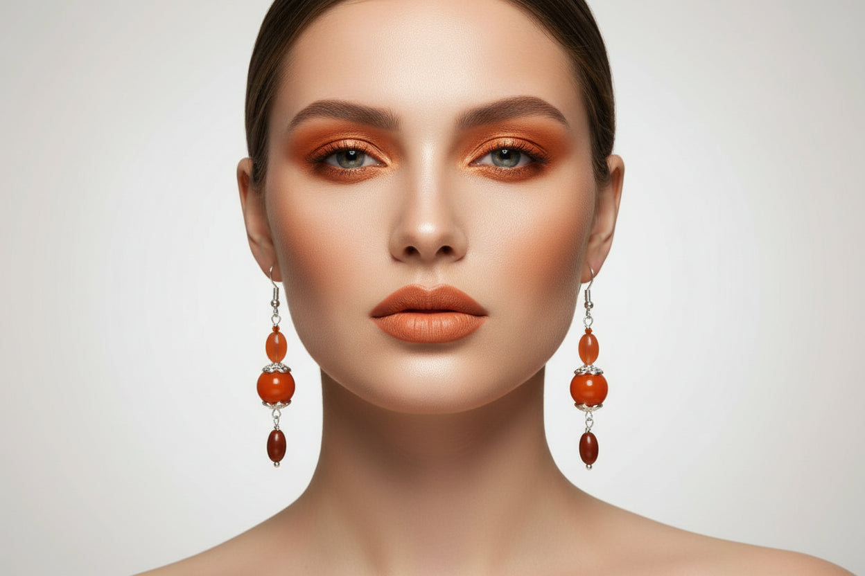 Pair of orange bead earrings hanging from a branch with a white background