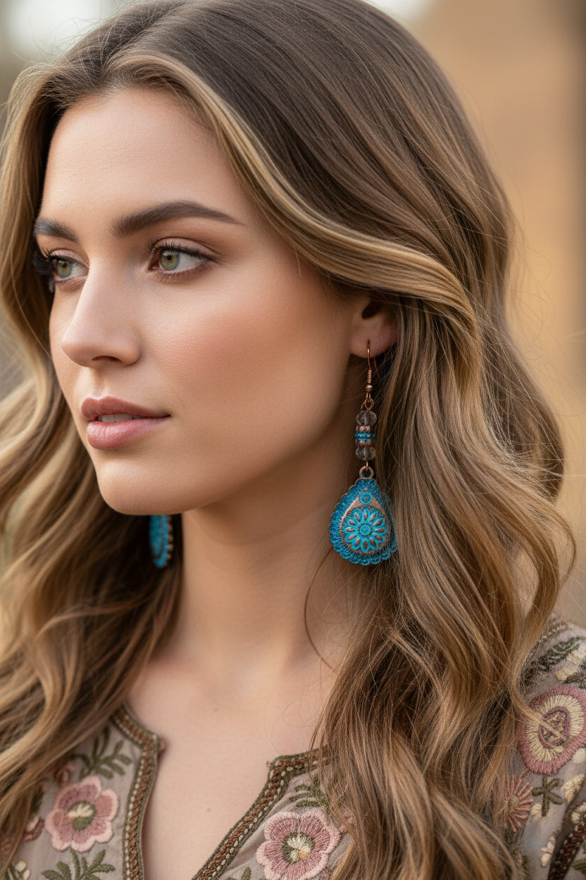 Blue floral earrings hanging from a branch on a white background