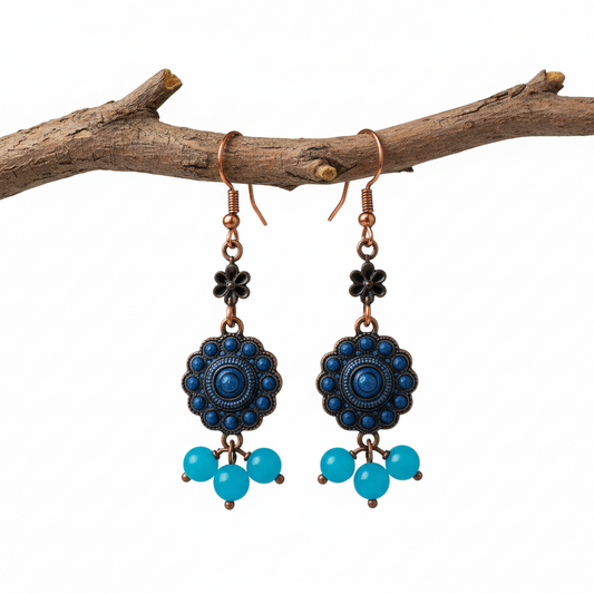 Pair of blue floral earrings with turquoise beads in front of a round light source on a gray background